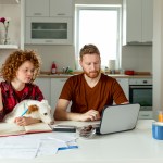 Couple does taxes at kitchen table with dog.